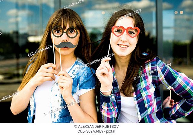 Portrait of two young women holding up mustache and eyeglass costume masks