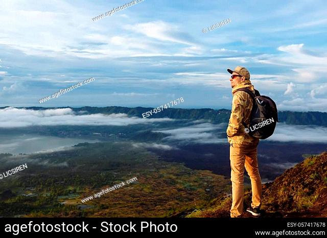 Man tourist looks at the sunrise on the volcano Batur on the island of Blai in Indonesia. Hiker man with backpack travel on top volcano