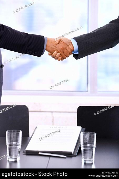 Business handshake in closeup over signed contract