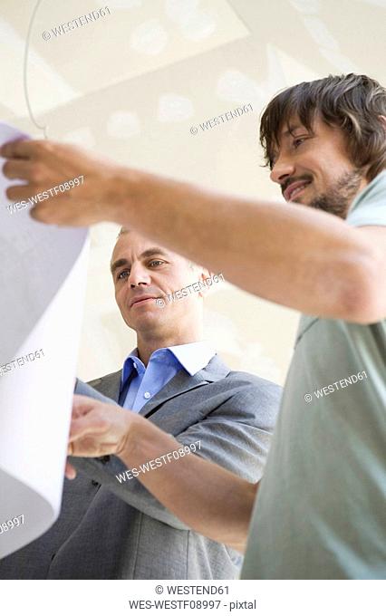 Two men looking at construction plan, smiling