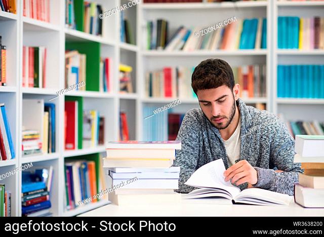 Portrait of happy student while reading book in school library. Study lessons for exam. Hard worker and persistance concept