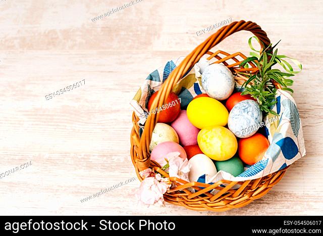 Polish traditional wicker basket full of multi coloured and mottled Easter eggs. Basket decorated with flowers on vintage oak table or background