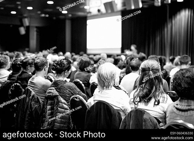 Business and entrepreneurship symposium. Speaker giving a talk at business meeting. Audience in conference hall. Rear view of unrecognized participant in...