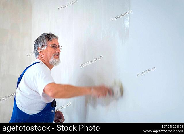 Senior man painting a room of rental appartment with a paint bucket, wall painting concept - short time rental property maintenance