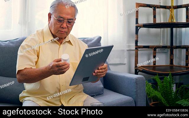 Asian elderly patient video call by digital tablet to doctor for inquire about which bottle of medication pills should be taken in living room at home