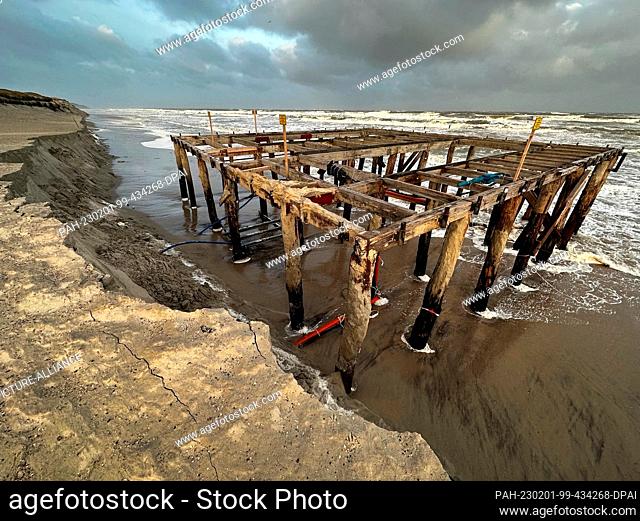 01 February 2023, Norderney: Waves wash around a wooden scaffold for changing rooms and lifeguards at the ""Weiße Düne"" beach section during stormy weather