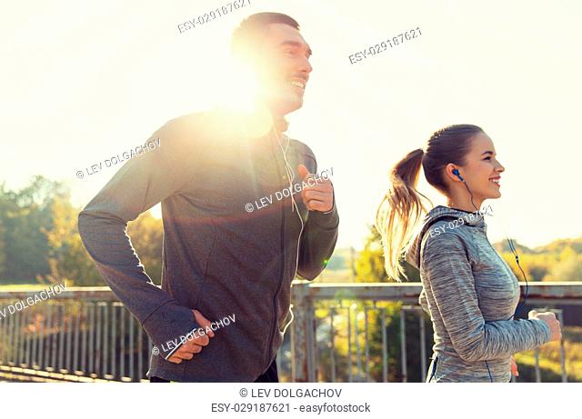 fitness, sport, people and lifestyle concept - happy couple with earphones running outdoors