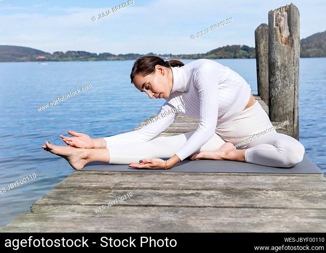 Woman doing stretching exercise on jetty at lake