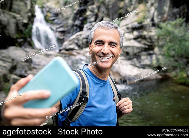 Smiling mature man taking selfie through mobile phone in forest
