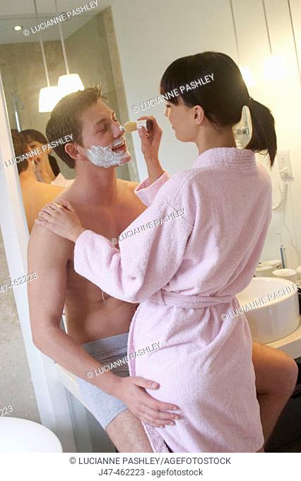 young couple standing together in underwear in the bathroom, shes helping him shave