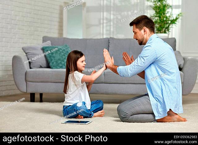 Little child girl plays with father at home sitting on white carpet