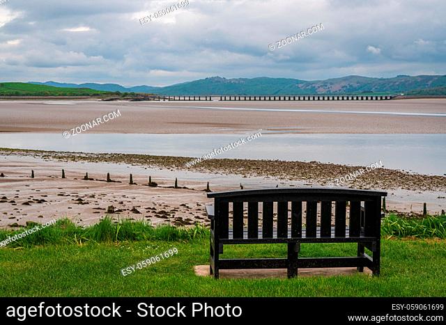 A bench overlooking the low tide at Morecambe Bay with Leven Viaduct in the background, seen from Canal Foot, Cumbria, England, UK
