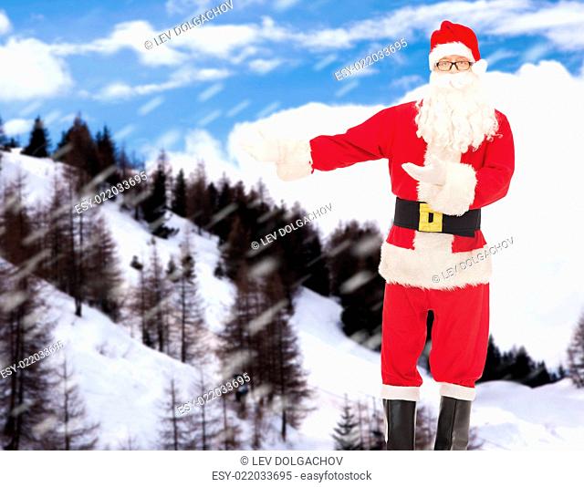 christmas, holidays, gesture and people concept - man in costume of santa claus over snowy mountains background