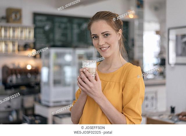 Young business owner standing in her coffee shop, drinking coffee