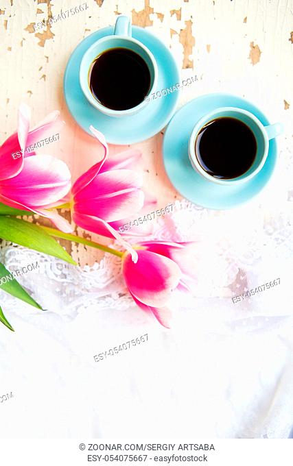two cups of coffee and pink tulips on an old table