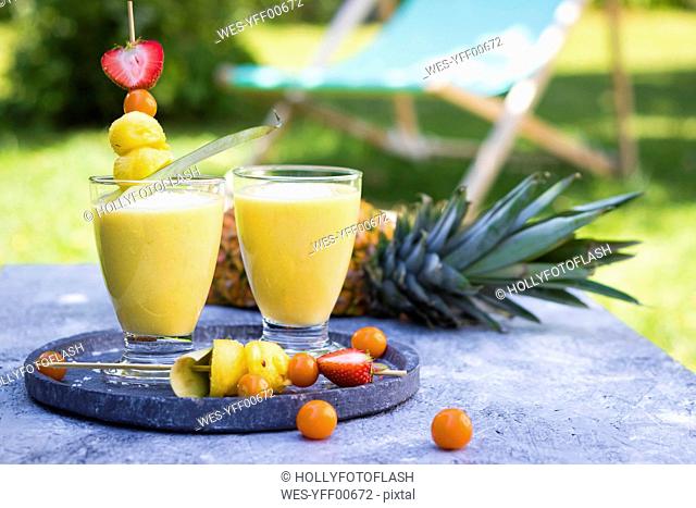 Two glasses of tropical smoothie with pineapple, mango, coconut milk and coconut flakes