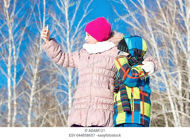 Two happy kids making selfie photo in winter park