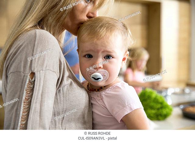 Portrait of female toddler in mothers arms in kitchen