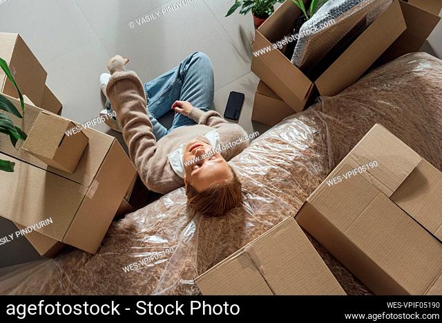 Tired woman resting on plastic wrapped bed at new home