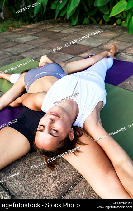 Yoga coach exercising with teenage girl lying on mat in park