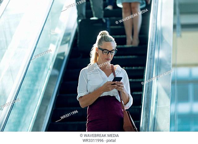 Caucasian businesswoman looking at mobile phone while using escalators in modern office