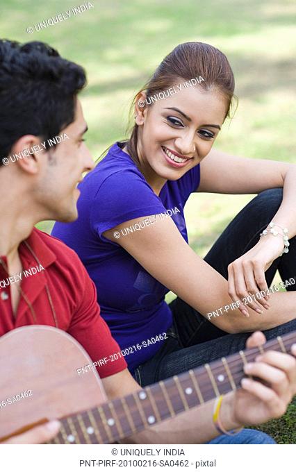 Man playing a guitar with a woman sitting beside him