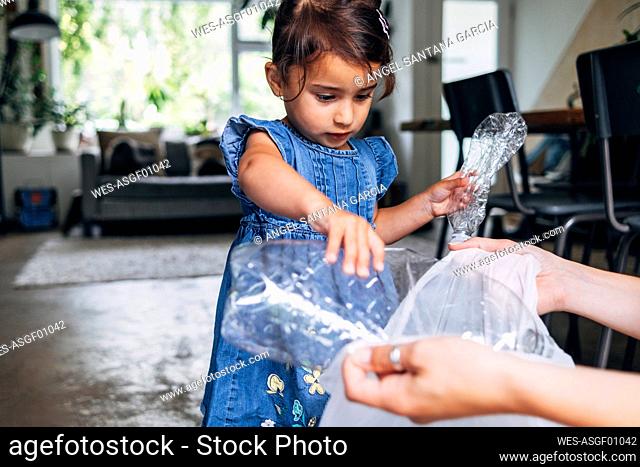 Girl helping daughter collecting crushed plastic bottle in garbage bag at home