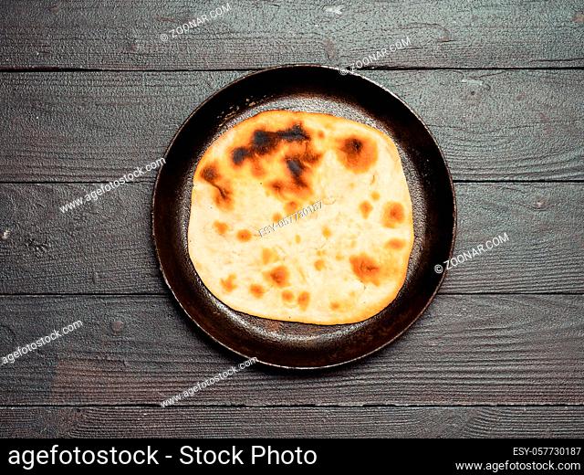 Fresh naan bread in cast-iron pan on dark wooden background with copy space. Top view of perfect naan flatbread black circle cast iron pan