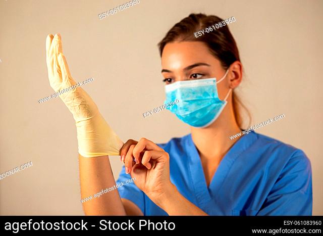 Young female nurse with blue surgical mask wearing protective rubber gloves. Concept of healthcare during pandemic of coronavirus