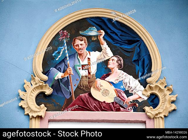 Woman playing a lute in front of greeting man with hat and stick. Lüftl painting on house facade in Mittenwald