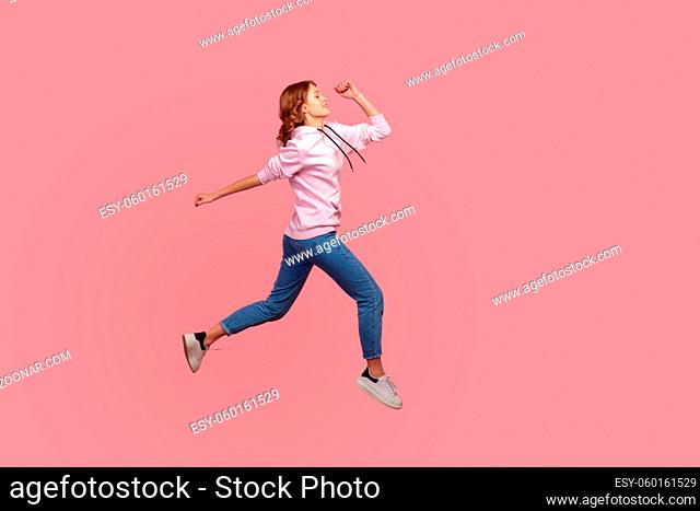 Full length side view of young female in hoodie and jeans running in air, hurrying for discounts, empty copy space for advertising