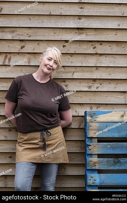 Portrait of waitress wearing brown apron, leaning against wall, smiling