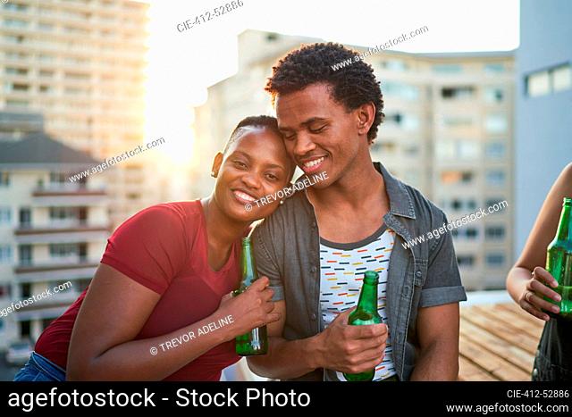 Portrait happy young couple drinking beer on sunny rooftop balcony