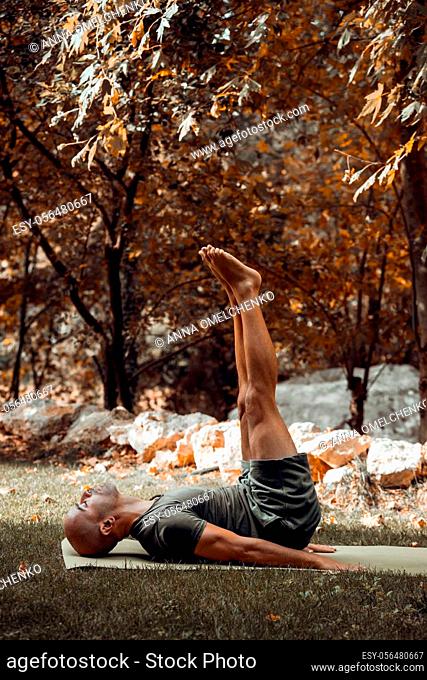 Handsome Sportive Man Doing Yoga in Autumnal Park. Athletic Guy Training Outdoors. Enjoying Peaceful Workout. Healthy Lifestyle