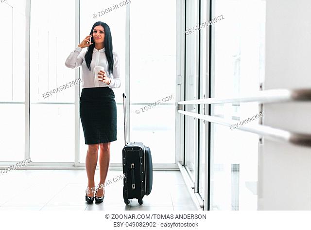 Successful confident young business woman with coffee and suitcase in an office setting