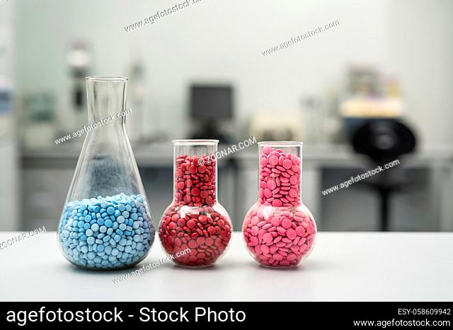 Three glass flasks with many colorful placebo pills on the light surface on the blurry background. Pills are blue, red, pink and have different size