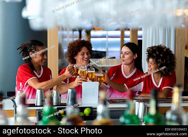 Diverse group of male and female sports fans raising glasses and watching game at bar