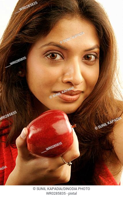 South Asian Indian teenager girl wearing red colour contact lenses in eyes and brown hair showing fresh red apple as fruit good for health MR686G