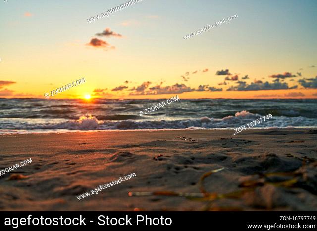 Sand am Strand bei Sonnenaufgang am Meer mit Wellen und Gischt morgens