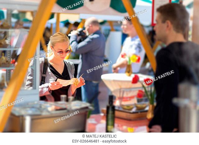 Beautiful blonde caucasian lady buying freshly prepared meal at a local street food festival. Urban international kitchen event in Ljubljana, Slovenia