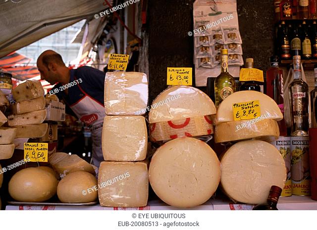 Market cheese stall with male stall holder displaying a selection of cheeses and euro money price signs