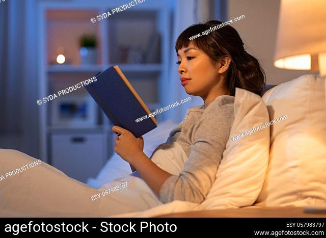 young asian woman reading book in bed at home