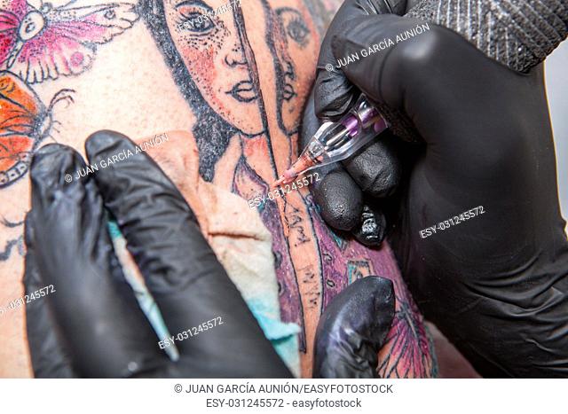 Tattoo artist applies tattoo to arm. She is filling with flesh-coloured ink the tattoo