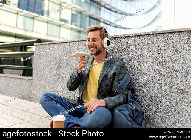 Happy man talking on speaker phone sitting by wall