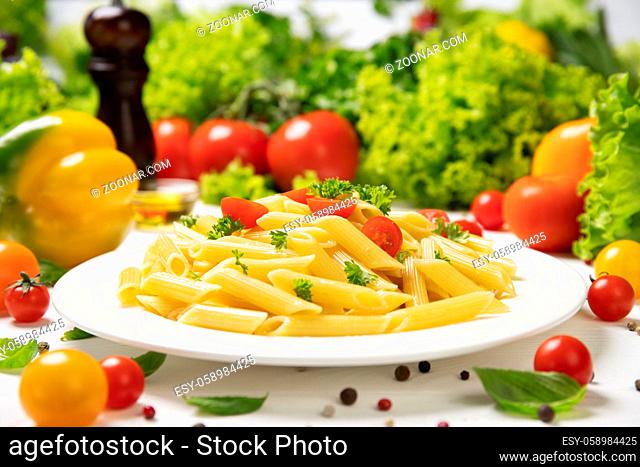 Plate of cooked italian pasta, penne rigate with tomatoes and basil leaves