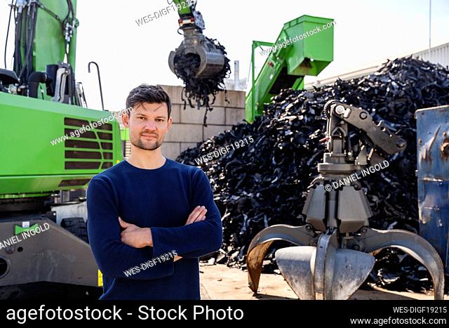 Businessman with arms crossed standing in front of excavator