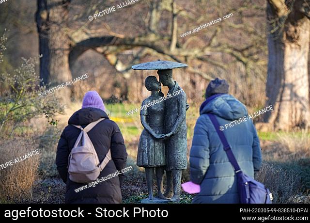 19 January 2023, Brandenburg, Potsdam: Two women contemplate the sculpture ""Lovers under the Umbrella"" (bronze, 1962) by Jürgen von Woyski in sunny but cold...