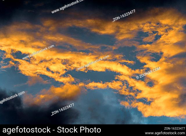 Golden fluffy clouds illuminated by disappearing rays at sunset and dark cumulonimbus floating across sunny blue sky to change season weather