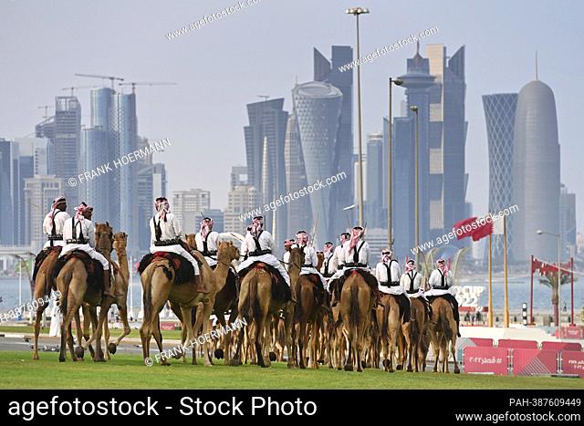 Impressions from Doha / Qatar on December 7th, 2022. Mounted camel guards on camels ride in front of the Doha skyline to the Amiri Divan seat of government of...