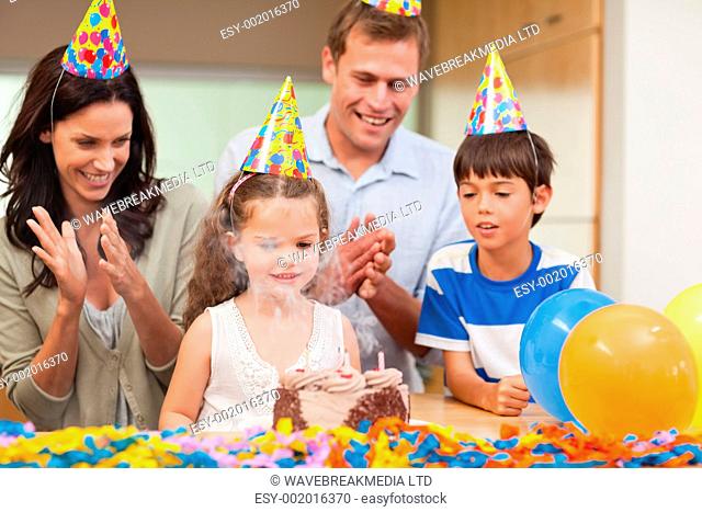 Parents applauding her little daughter who just blew out the candles on birthday cake